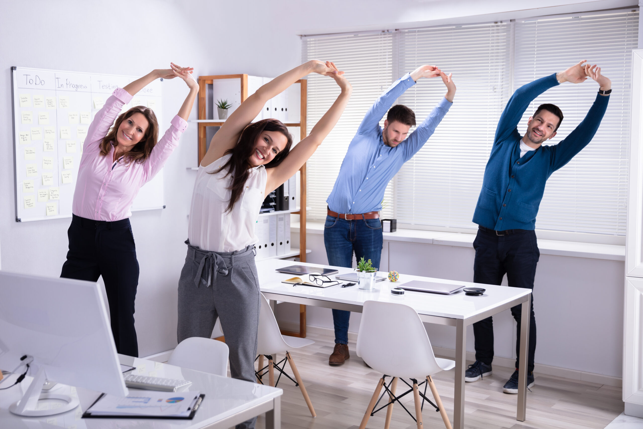Happy employee Doing Stretching Exercise Behind Desk At Workplace