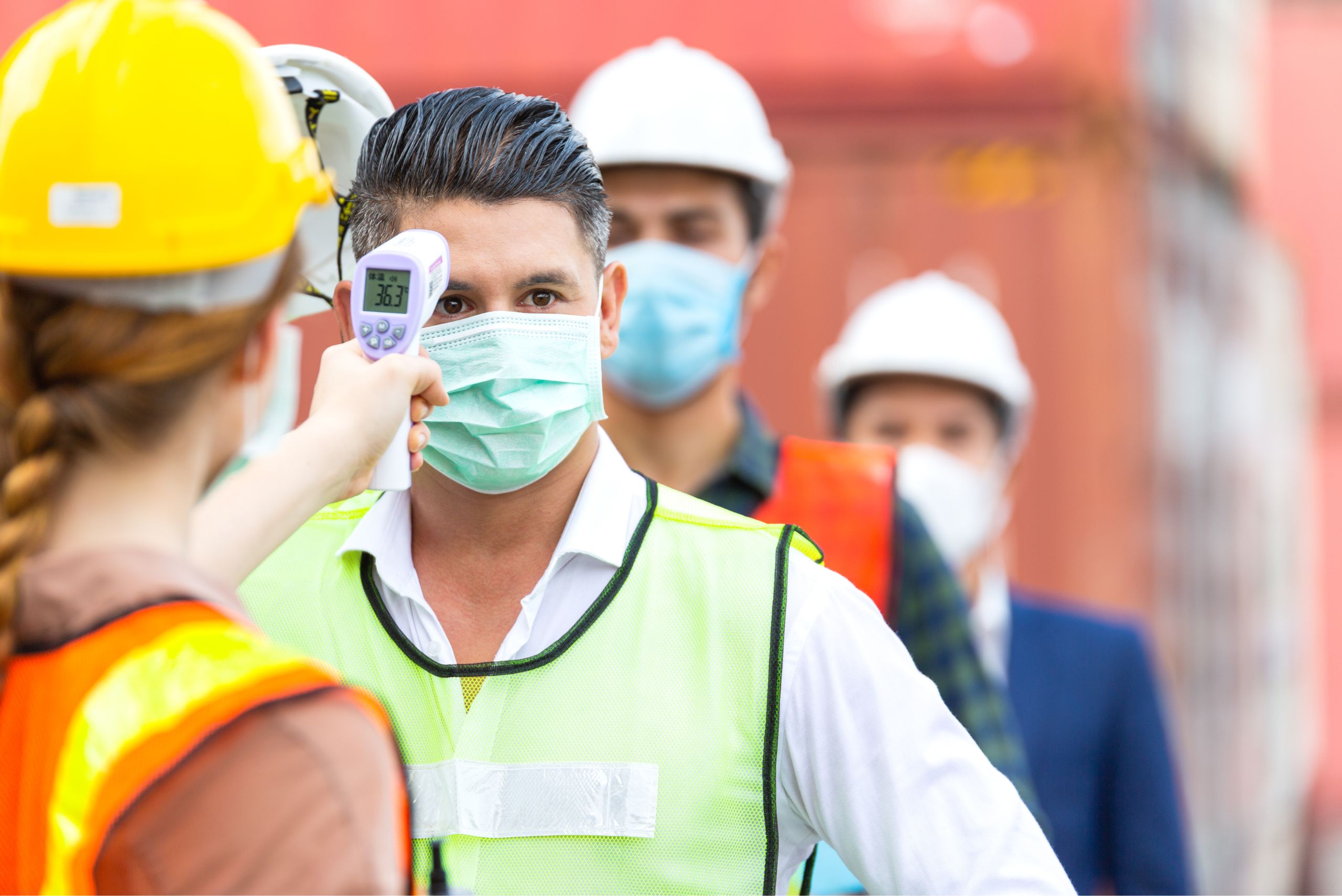 A female employee is using a temperature scanning device to check the construction worker's body temperature as part of their health and safety measures.
